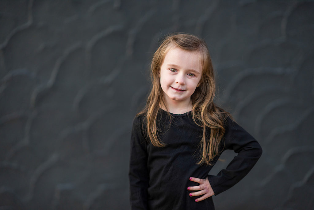 little girl in black shirt poses in front of black textured wall in Benton, Arkansas