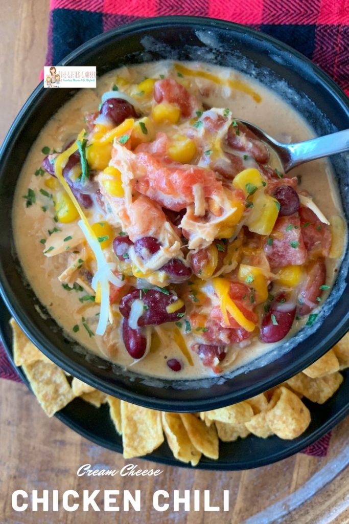 cream cheese chicken chili in black bowl with Fritos surrounding on plate