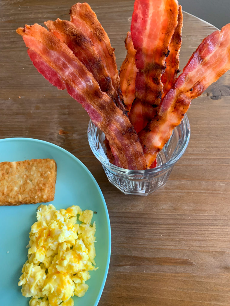 glass of grilled bacon standing upright and blue plate of eggs and hashbrowns