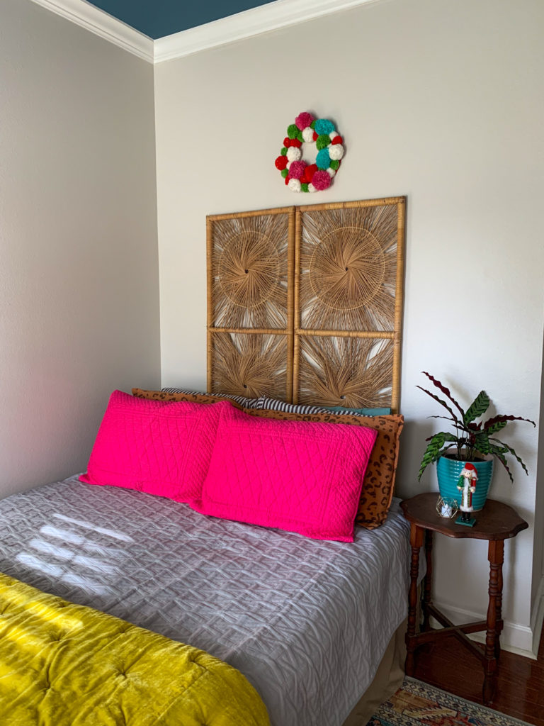 a colorful pom pom Christmas wreath over a bed in a guest room