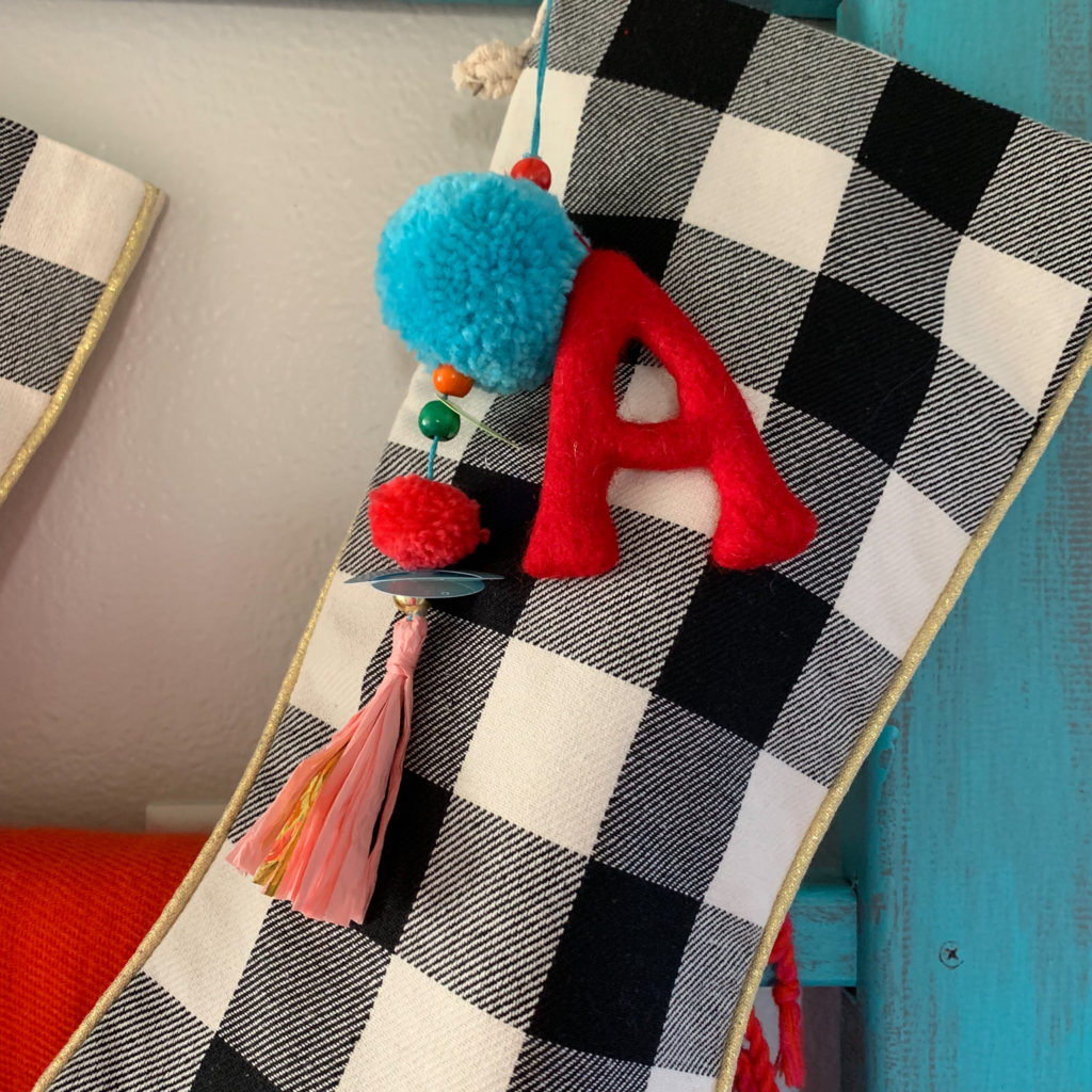 a black-and-white plaid stocking with a colorful pom pom tassle and an A initial