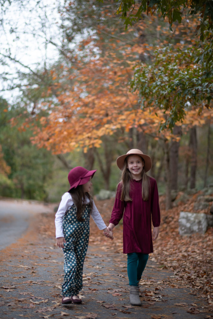 two little girls hold hands and laugh in Little Rock, Arkansas while wearing little girl floppy hats