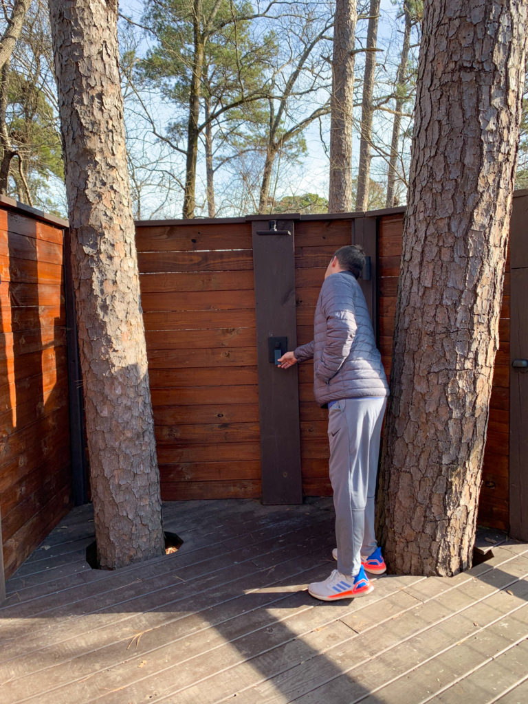 man explores outdoor shower in between two large pine trees