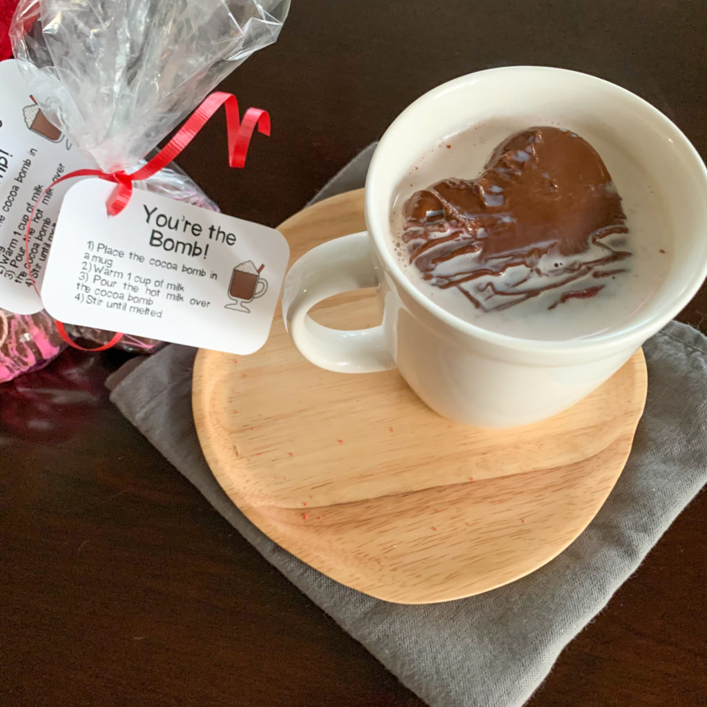 hot cocoa bomb in mug of milk on wooden plate with printable hot cocoa bomb gift tag in background