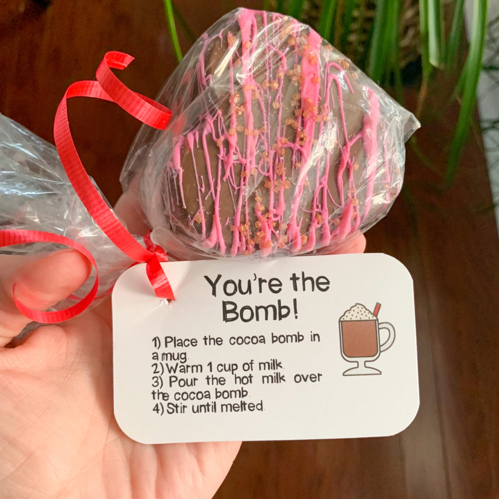 hand holding hot chocolate bomb in hand with a free printable hot cocoa bomb gift tags