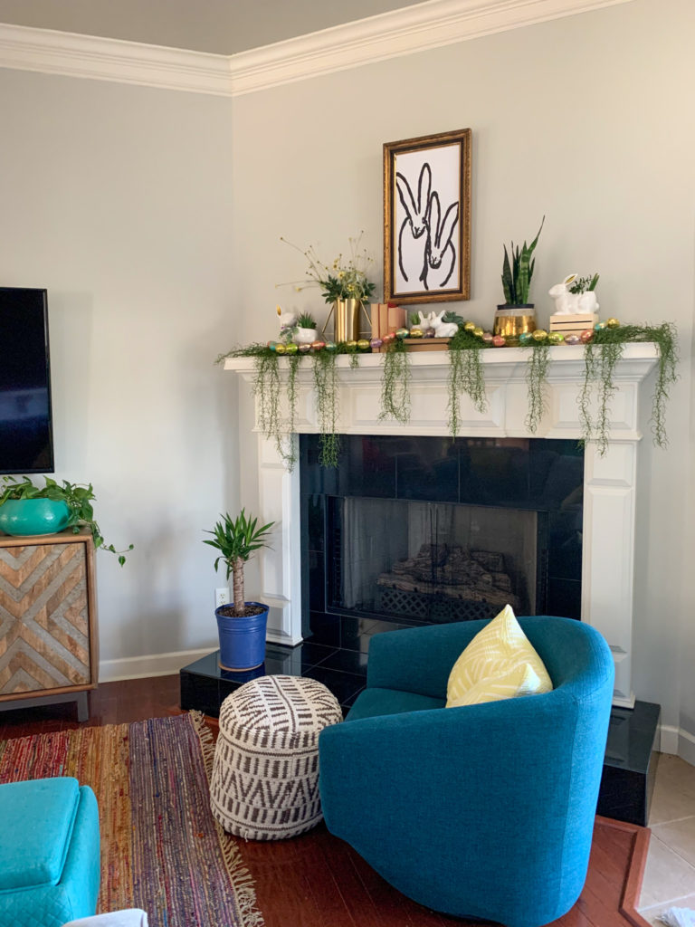 bunny decorative mantle with bunny painting wall art and bunny planters with plants and books with blue chair in front