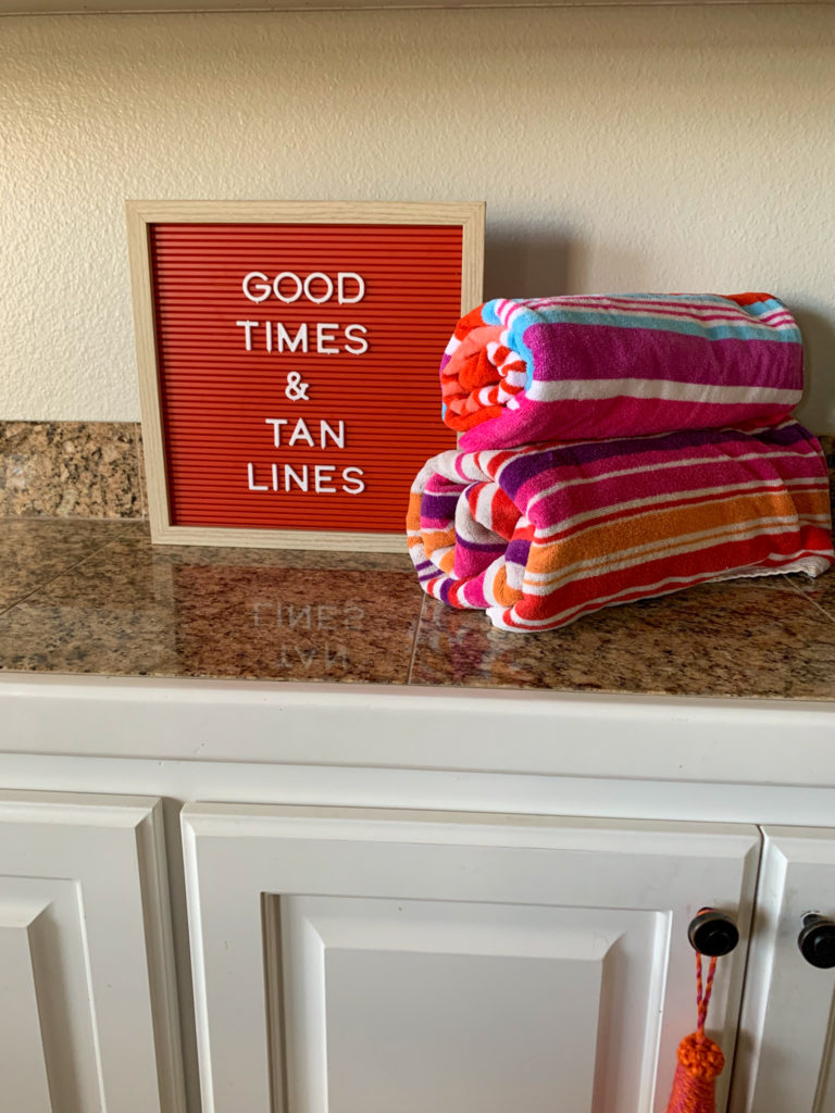 good times and tan lines - inspiring beach quotes on beach fun on red letter board with stack of beach towels on counter