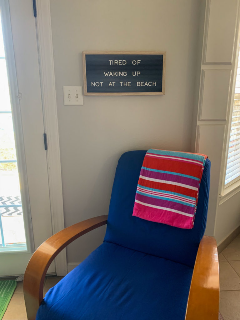 tired of waking up not at the beach summer letter board on wall above blue chair with colorful beach towel for inspiring beach quotes on beach fun