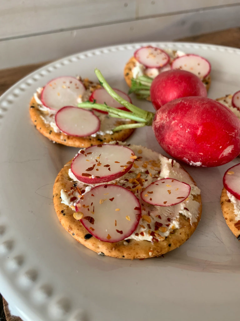 a white plate of Boursin cream cheese crackers with radishes with two red radishes in the center of plate