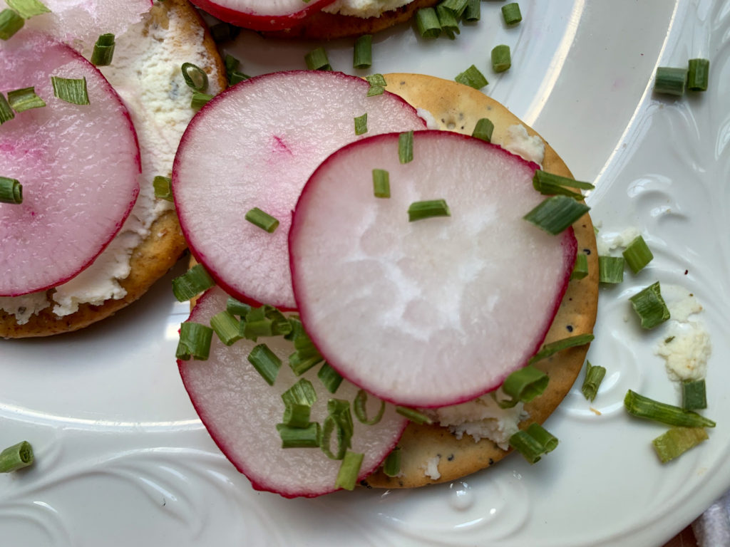 white plate with Cream cheese crackers with Boursin cream cheese spread topping, sliced radishes and chives