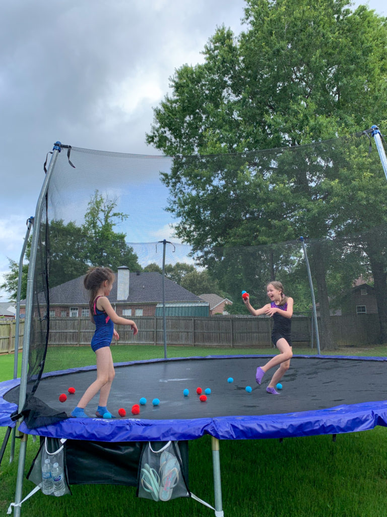 two girls playing with reusable water balls as a sort of fun trampoline ball game on an oval trampoline