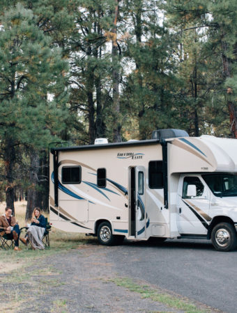 couple of RV owners sit in front of motorhome with their essential camping gear