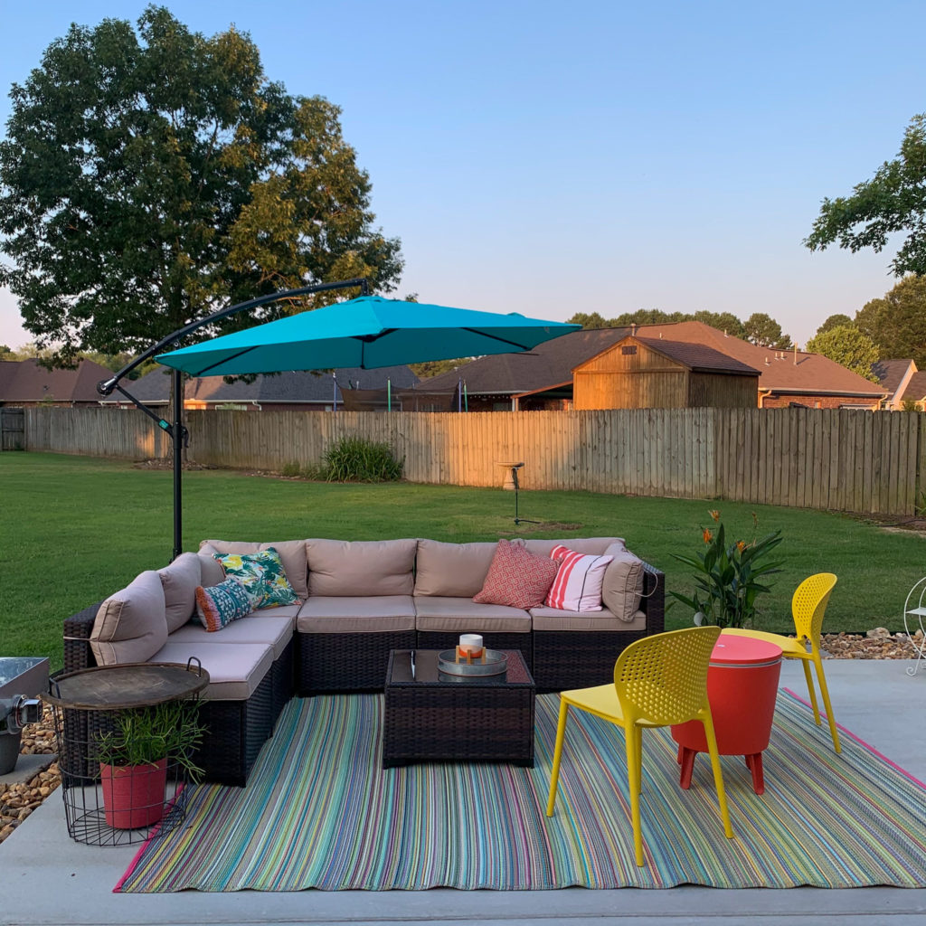 yellow Article dot chairs, patio cooler table combo with outdoor wicker sectional and teal umbrella over concrete slab