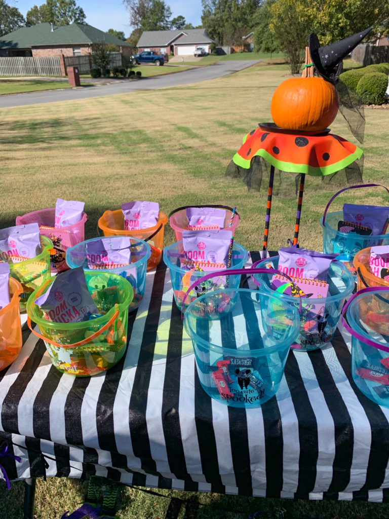 a Halloween table with tubs of candy and a pumpkin on a Halloween plant stand 