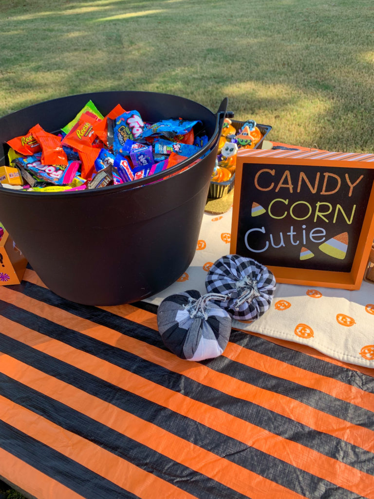 an outdoor Halloween party table with a kettle pot of candy and a Candy corn cutie sign