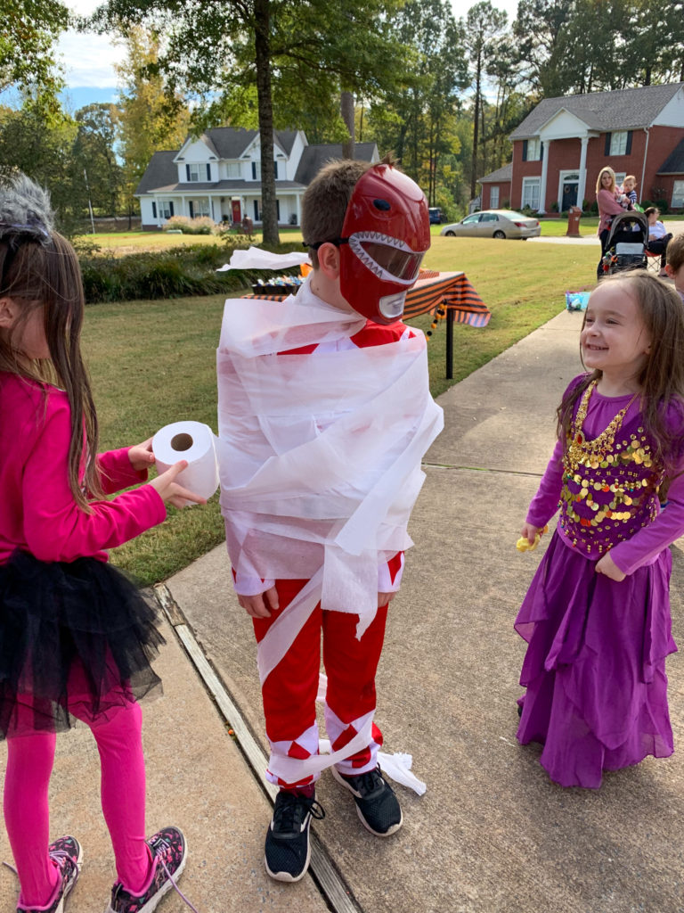 three children playing a toilet paper mummy game in a driveway