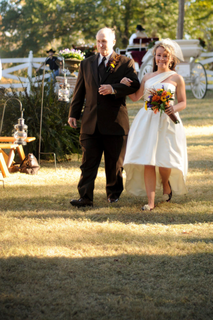 woman wears a custom wedding dress made by her mother as she walks down the aisle with her father at Alda's Magnolia Hill, one of the popular Arkansas wedding venues