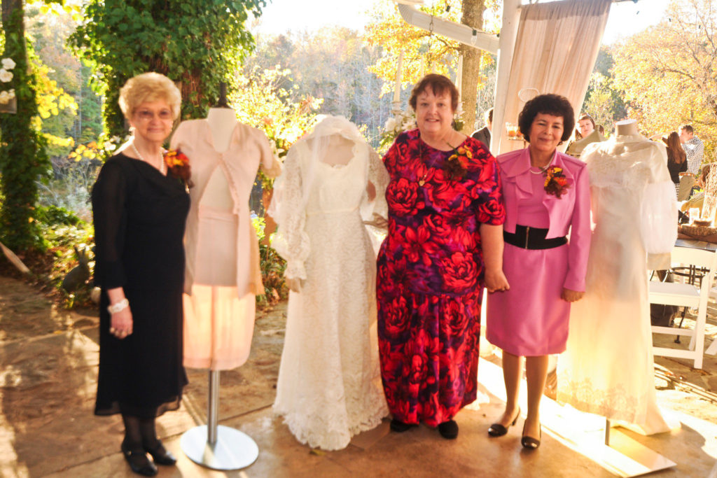 two mothers and a grandmother of the bride and groom stand beside their heirloom wedding gowns at their children's wedding at Alda's Magnolia Hill