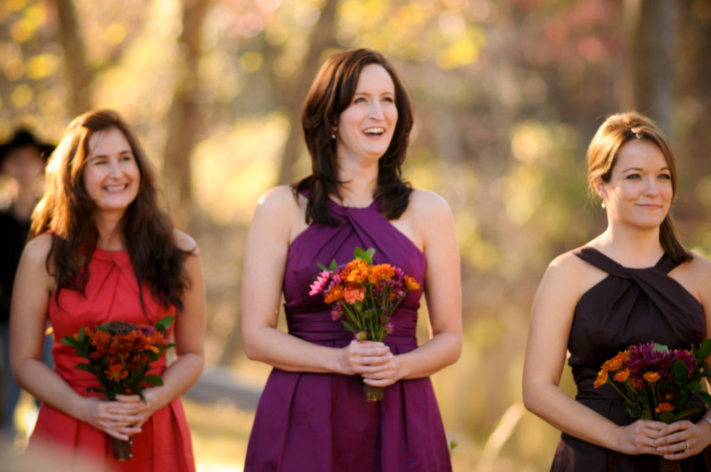 three bridesmaids wear rustic wedding colors dresses - persimmon, plum, and chocolate - while holding fall bouquets