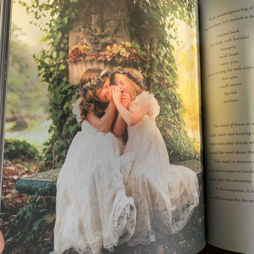 a copy of Alda Ellis' wedding planner book lays open to a page with two flower girls whispering and laughing