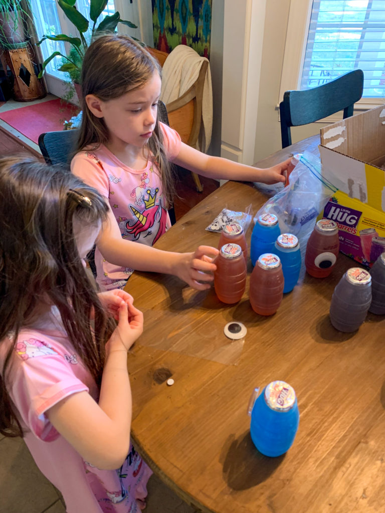 two little girls make Halloween juice boxes at kitchen table