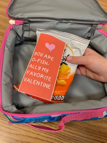 child holds a free printable Valentines lunch box note attached to a bag of Gold Fish lunch box snack