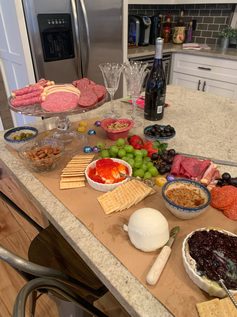 potluck charcuterie table with wine bottle and wine glasses in back