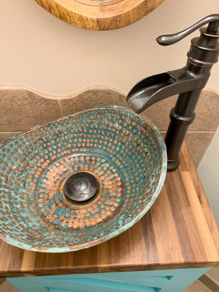 a Moroccan hammered copper sink on a custom turquoise vanity with a stained walnut vanity top and waterfall faucet