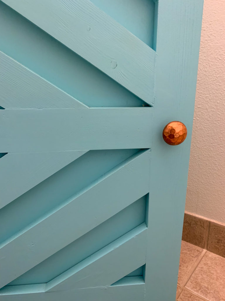 a handmade bathroom vanity painted turquoise with a hammered copper cabinet knob 