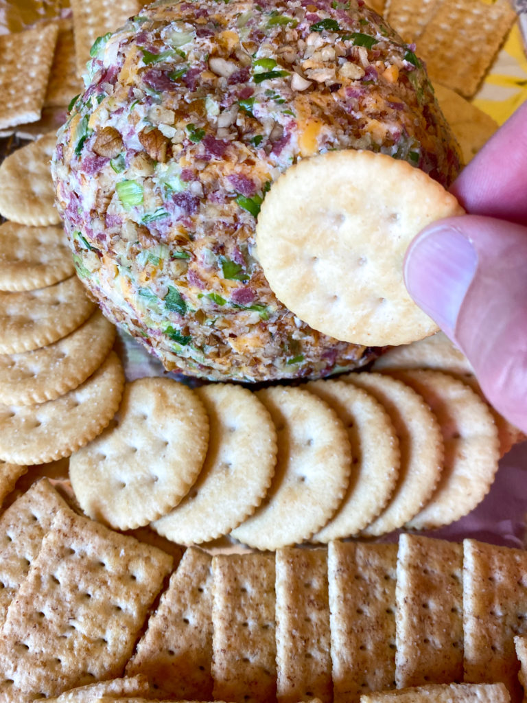 man dips cracker into cheese ball with dried beef 