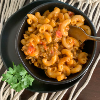 cheesy beef goulash on black plate with green garnish to side