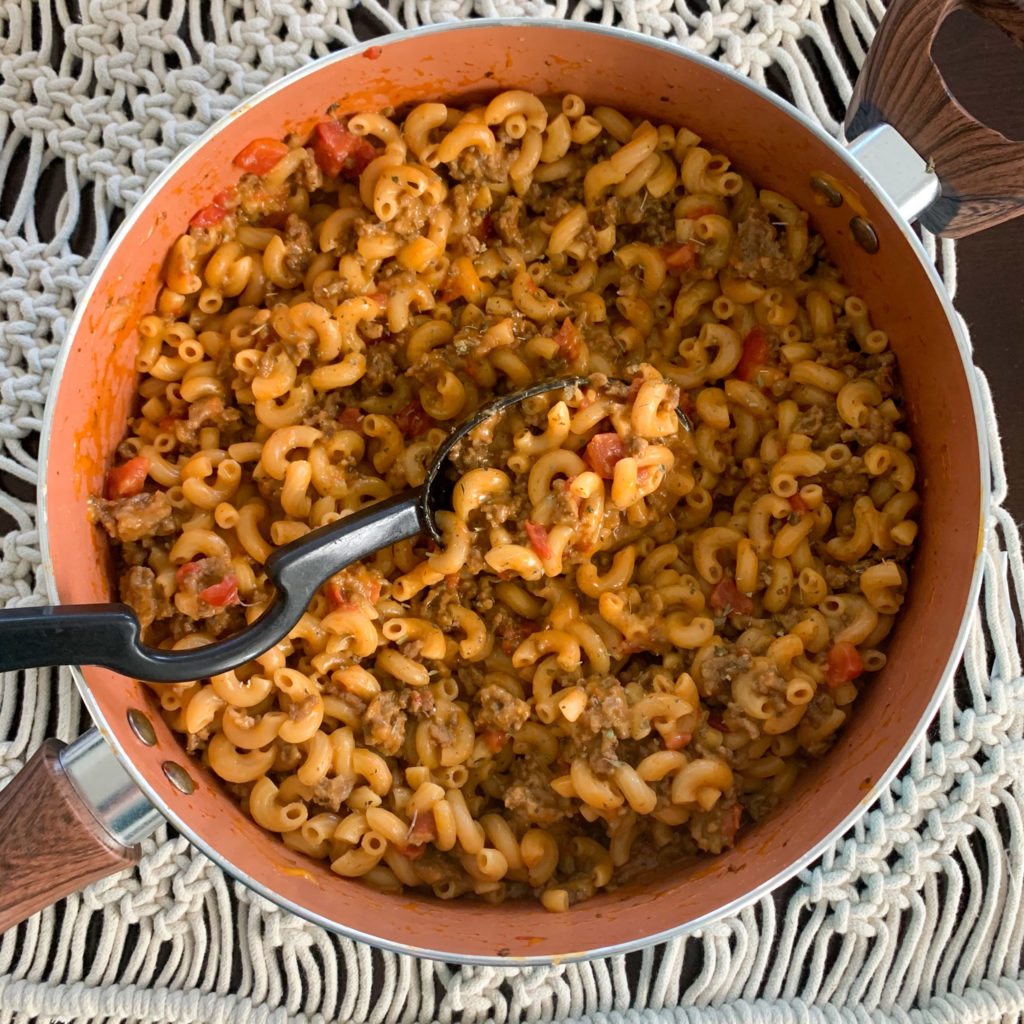 overhead shot of cheesy beef goulash in skillet with black serving spoon