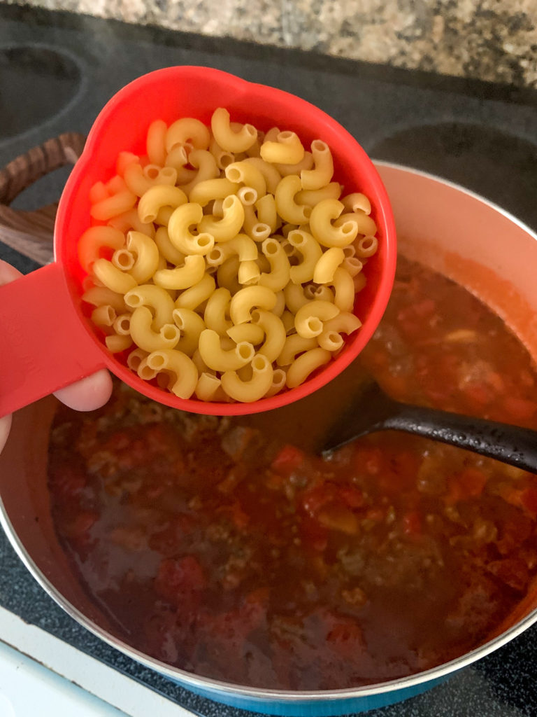 uncooked elbow macaroni about to pour into pot of beef and macaroni skillet