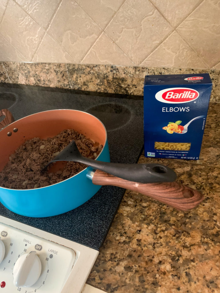 ground beef in pot with a box of pasta Elbows on right