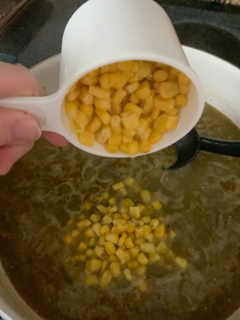 cup of whole kernel corn poured into pot of salsa verde with pasta