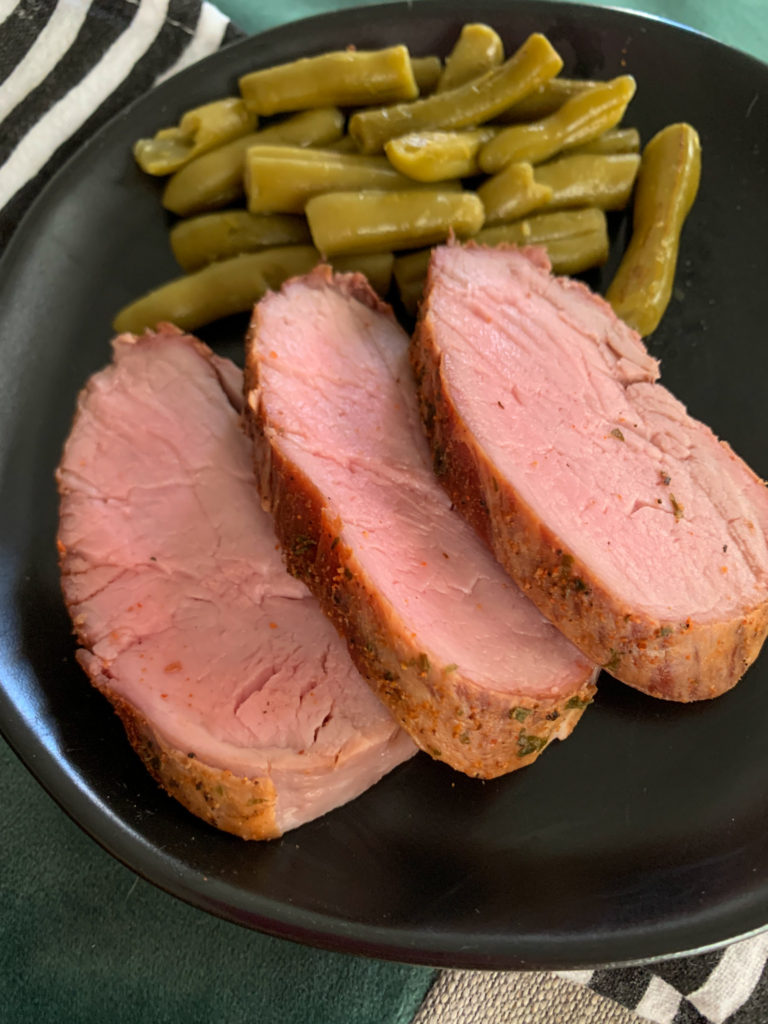 three slices of smoked pork tenderloin medallions on black plate with green beans