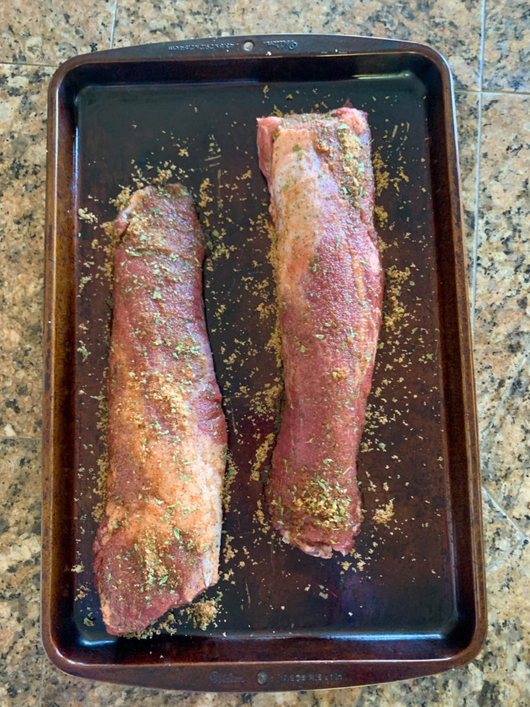 two raw pork tenderloins on a baking sheet on a brown counter