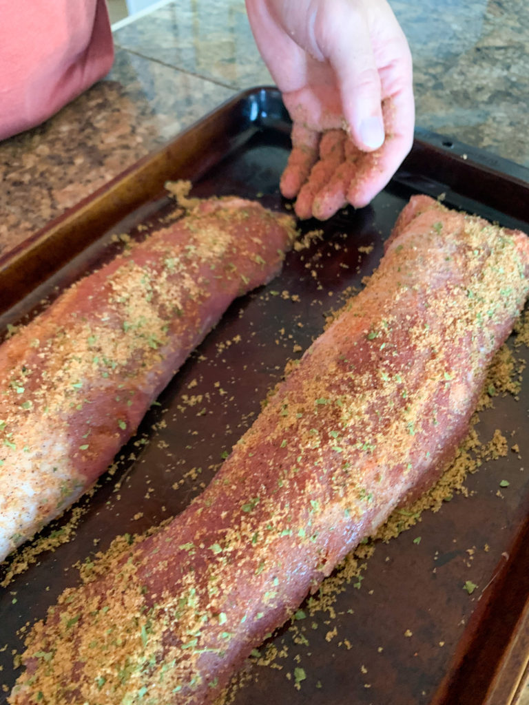a man rubs seasoning on two pork tenderloins on a baking sheet for smoker pork tenderloins