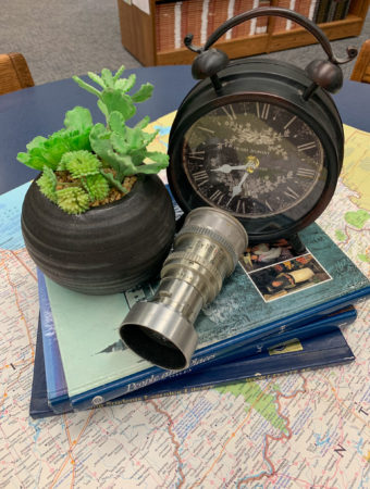 a vintage inspired travel theme centerpiece with a potted succulent, an old clock, and a stack of books