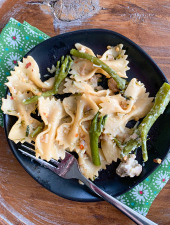 sausage broccolini pasta on black irregular plate with floral napkin