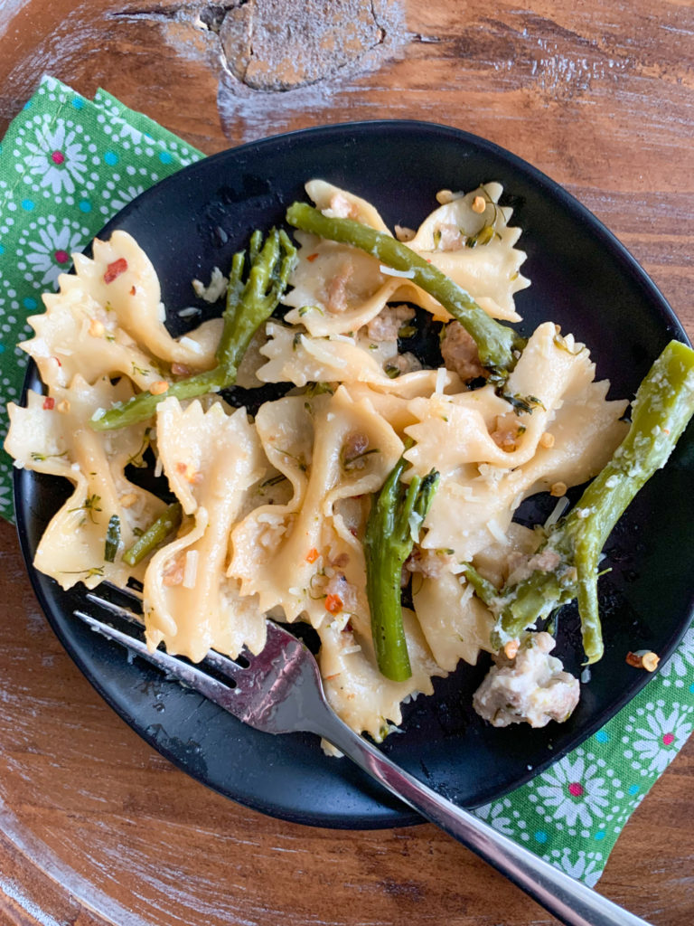 sausage broccolini pasta on black plate with green floral napkin 