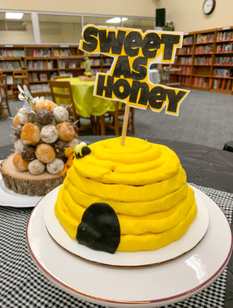 honey bee baby shower cake on white platter with "Sweet as Honey" cake topper