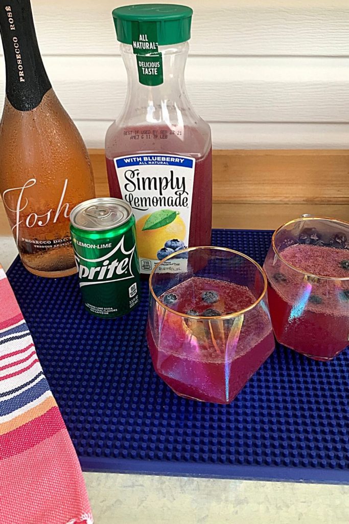 two glasses of Simply Blueberry Lemonade with Prosecco in wine glasses on patio bar with ingredients in background