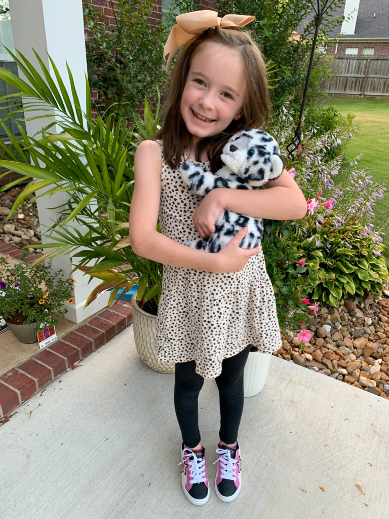 girls wears Animal Kingdom outfit ideas with cheetah dress while holding her snow leopard stuffed animal from Animal Kingdom