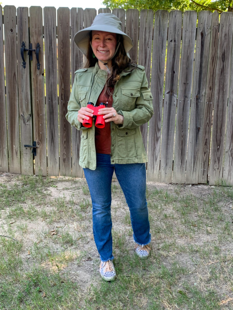 woman wears safari hat and safari jacket for Animal Kingdom outfit ideas while holding red binoculars