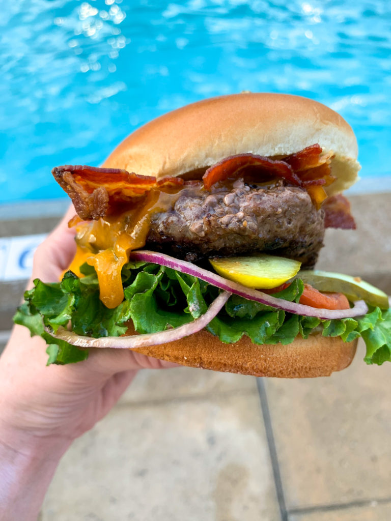woman holds cheeseburger from Spyglass Grill in front of pool 