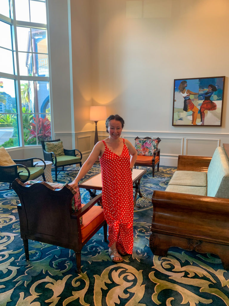 woman in red and white polka dot dress stands in Old Port Royale lobby at Disney Caribbean Beach Resort