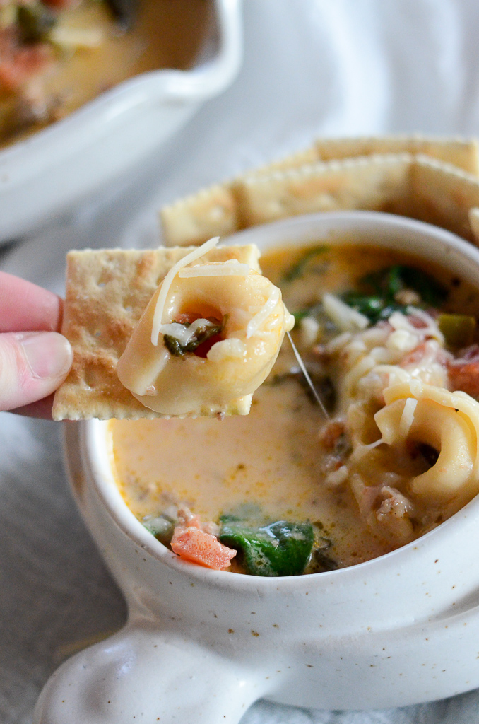 woman dips cracker into Jimmy Dean sausage tortellini soup with spinach and tomatoes in white vessel 
