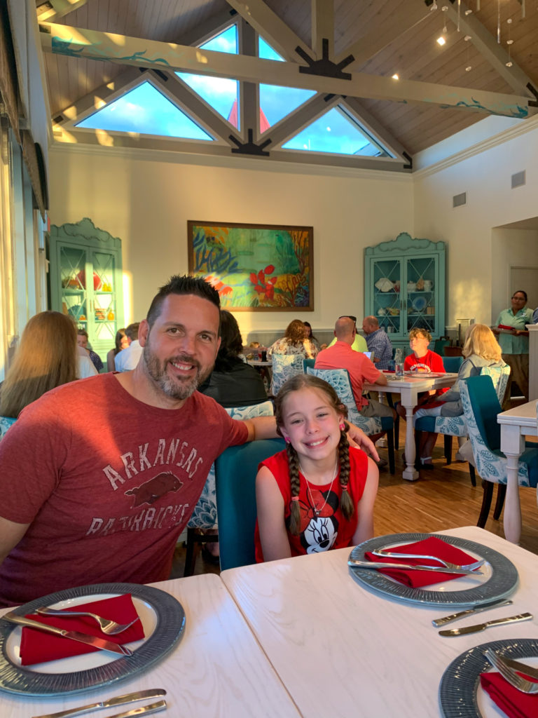 father and daughter smile at table in Sebastians Bistro during a stay in Disney Caribbean Beach Resort pirate room and property