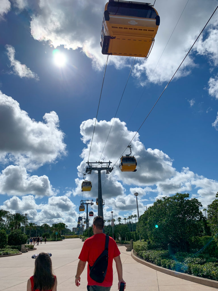 child and man walk under Disney World Skyliner gondola system